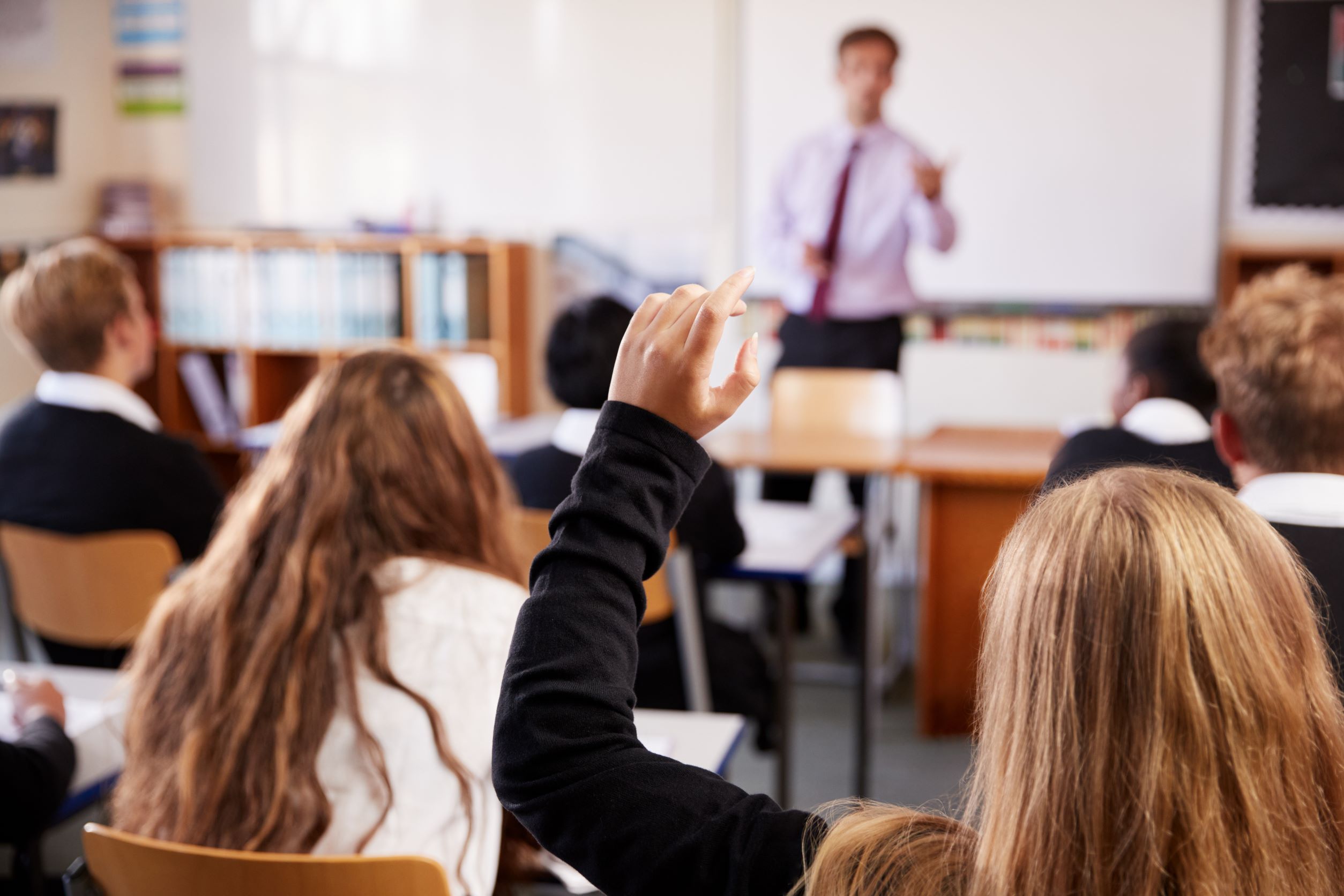 Schoolchild raises hand in a classroom with teacher